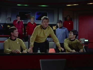 Bridge of Enterprise and crew. In ceneter is a diseveled Captain Pike leaning on the navigation console flanked by Sulu and unknown pilot both sitting. Behind is Spock observing, and three security members in the background.