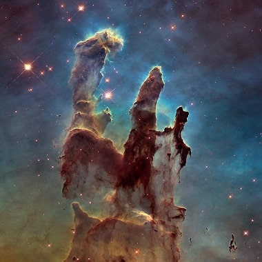 The pillars of creation, a famous image of a dust cloud in distant space that almost looks like a ghostly hand reaching up with light blue gas clouds and stars as a backdrop.